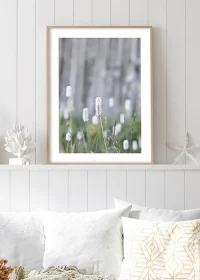 Poster mit Frühlingsgräsern über einem weißen Sofa an eine Holzwand gelehnt