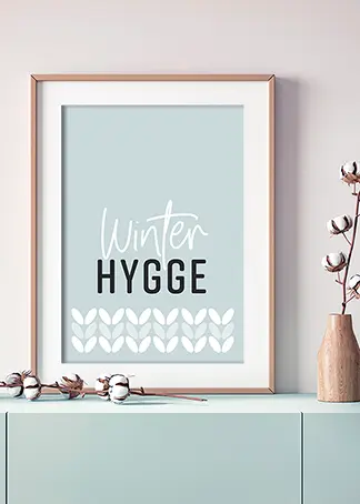 Poster mit Typografie "Winter-Hygge" in eisblau auf einem Sideboard stehend