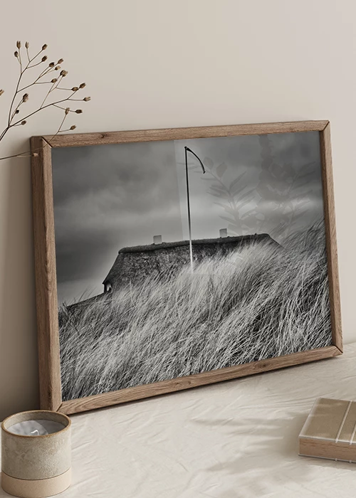 Poster mit einem Haus in den Dünen in schwarz-weiß an eine Wand gelehnt
