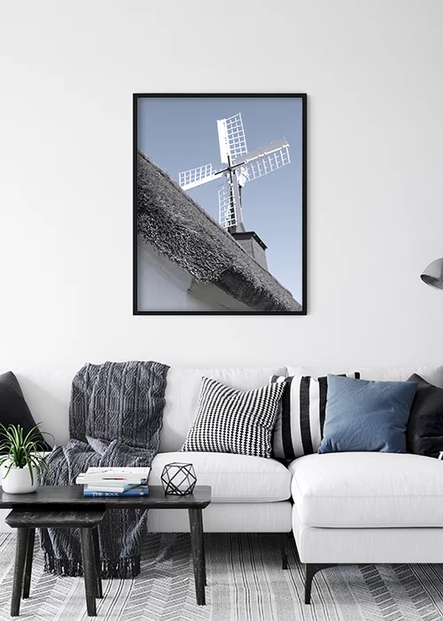 Poster mit einer Windmühle vor blauem Himmel über einem Sofa hängend