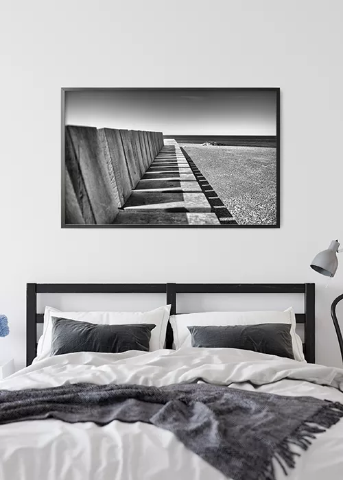 Poster mit einer Bank am Meer in schwarz-weiß über einem Bett hängend