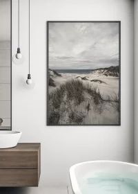 Poster mit Blick von einer Düne auf das Meer mit dramatischem Himmel in einem Badezimmer hängend