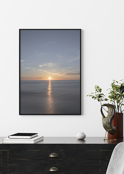 Poster mit untergehender Sonne über dem Meer über einer Kommode hängend