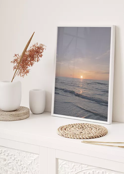 Poster mit untergehender Sonne über dem Meer auf einem weißen Sideboard stehend