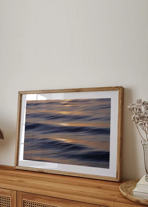 Poster mit Wellen auf dem Meer in der goldenen Abendsonne auf einem Sideboard stehend