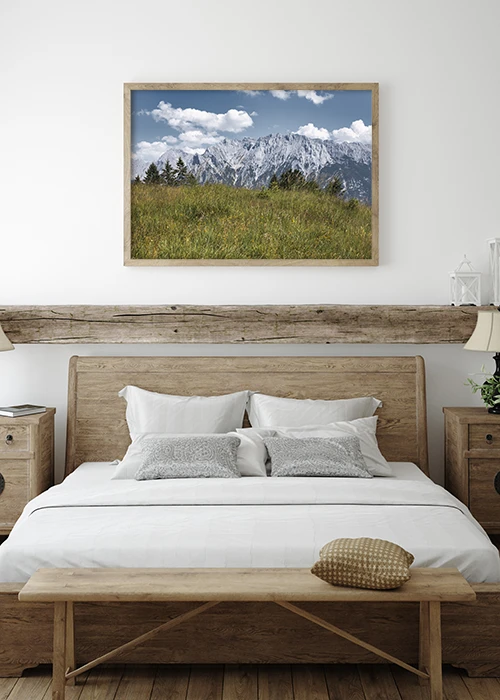 Poster mit Blick über eine grüne Sommerwiese auf die Alpen über einem Bett hängend