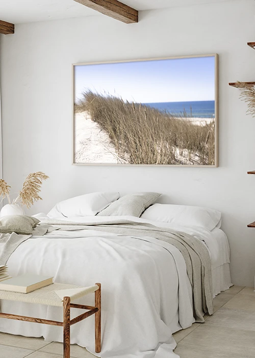 Poster mit Gras in den Sanddünen und dem Meer im Hintergrund über einem Bett hängend