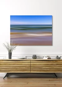 Poster mit abstrakter Darstellung von Strand und Meer unter einem blauen Himmel über einem Sideboard hängend