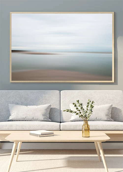 Poster mit abstrakter Darstellung von Strand, Meer und Himmel über einem Sofa hängend
