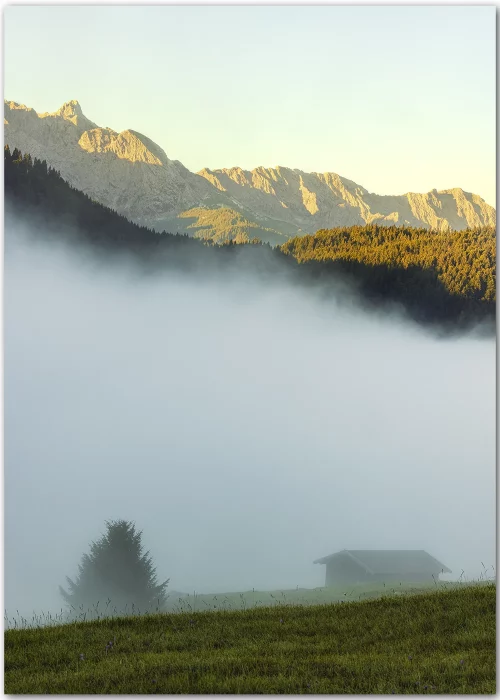 Poster mit einer im Nebel liegenden Alm und in der Sonne leuchtenden Berggipfeln