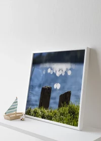 Poster mit Lichtpunkten auf der Wasseroberfläche eines Sees in Nahaufnahme auf einem Sidesboard stehend an die Wand gelehnt