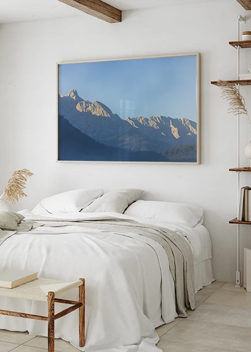 Poster mit in der Morgensonne leuchtenden Berggipfeln in blau-grauer Farbstimmung über einem Bett hängend