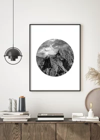 Poster mit stylisher Abbildung von Berggipfeln unter einem dramatischen Himmel in einem Kreis über einem Sideboard hängend