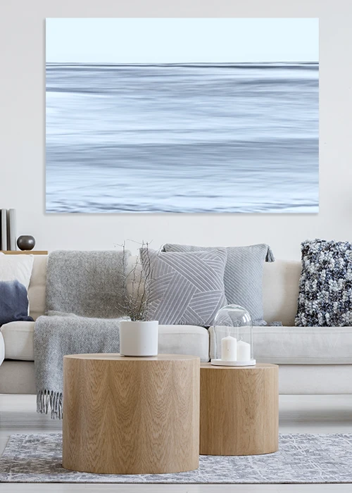 Wandbild AluDibond® mit einer ruhigen Meeresoberfläche in zartem Blau über einem Sofa