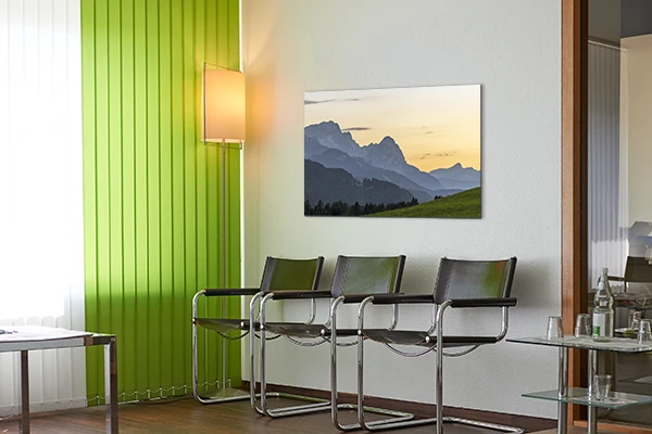 Ein alpines Wandbild mit dem Zugspitzmassiv in der Abenddämmerung – Wartezimmer einer Arztpraxis.