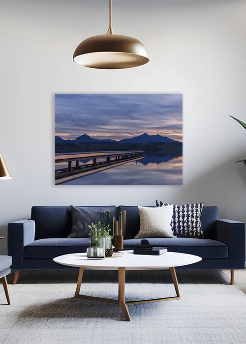 Inspiration – Wandbild mit einem Badesteg an einem See mit Bergpanorama, aufgehängt über einem Sofa.